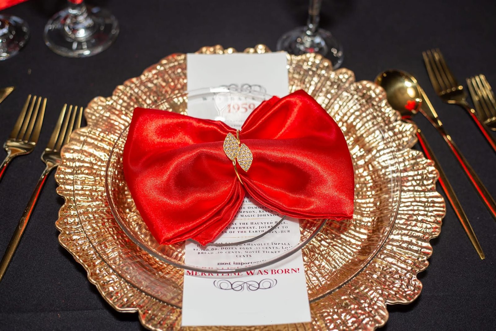 Red satin napkin tied in a bow with a jeweled ring on a gold charger